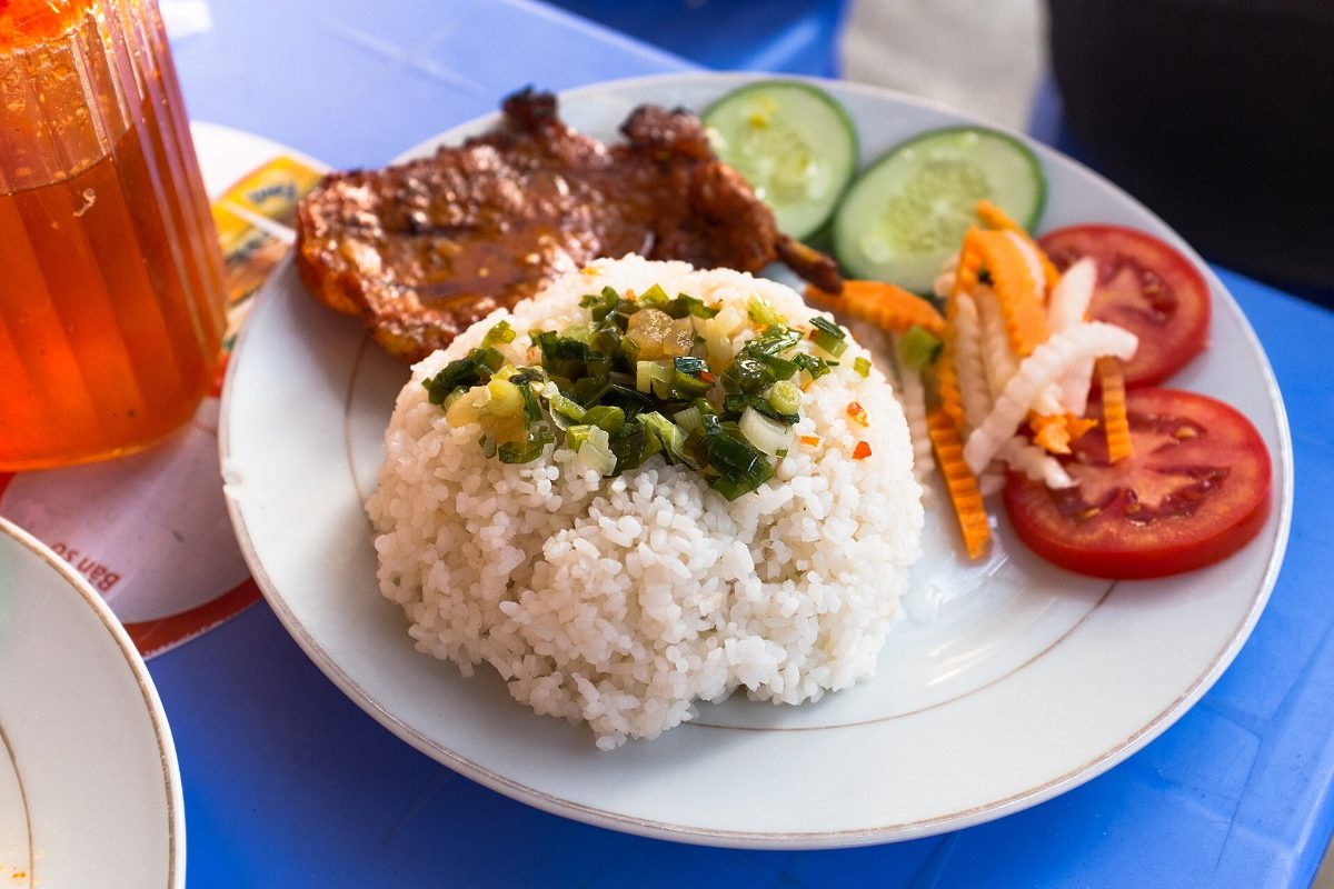 Plate of com tam broken rice with grilled meat, spring onion oil, tomato and cucumber