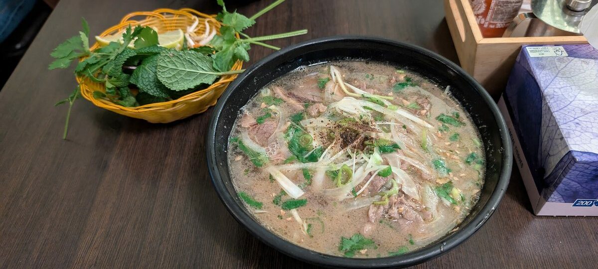 Bowl of beef pho (pho bo) with fresh herbs, lime and chilli
