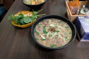 Bowl of beef pho (pho bo) with fresh herbs, lime and chilli