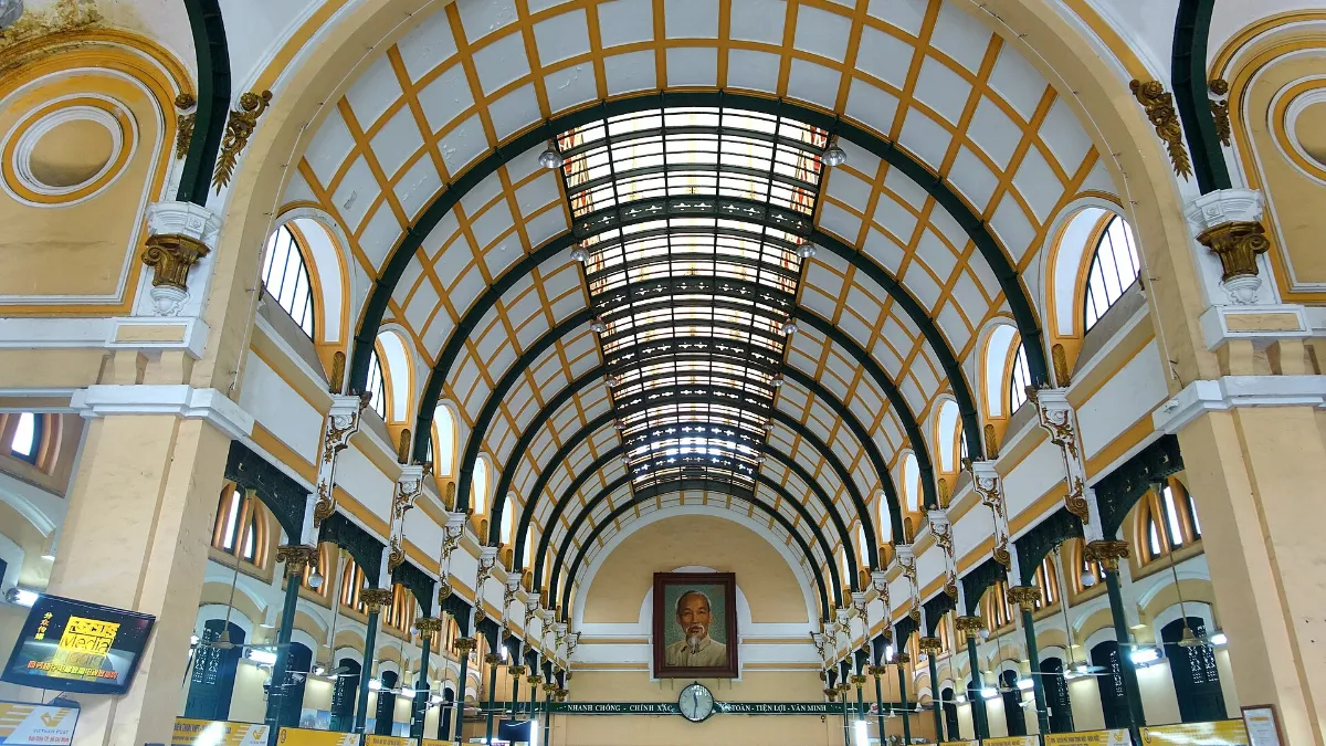 Vaulted main hall of Saigon Central Post Office with iron arches and the portrait of Ho Chi Minh